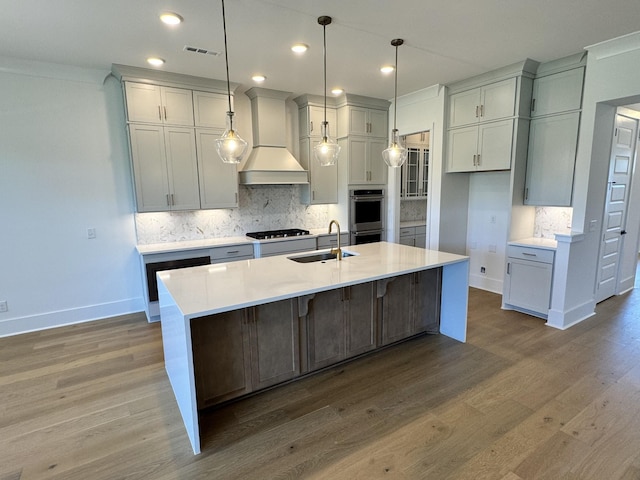 kitchen with tasteful backsplash, custom range hood, a sink, gas cooktop, and wood finished floors