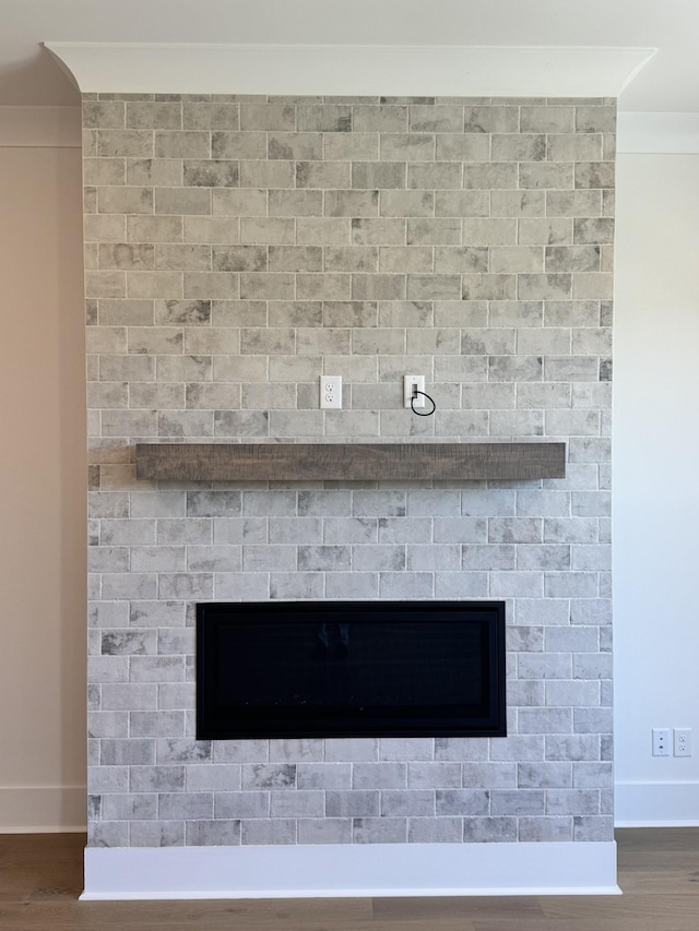 room details with baseboards, wood finished floors, a large fireplace, and crown molding