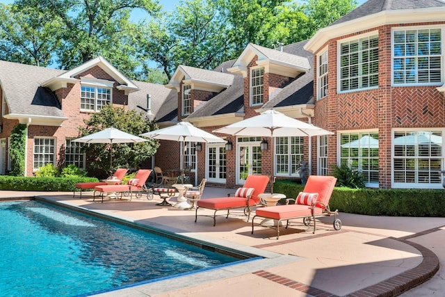 back of property featuring an outdoor pool, a patio area, roof with shingles, french doors, and brick siding