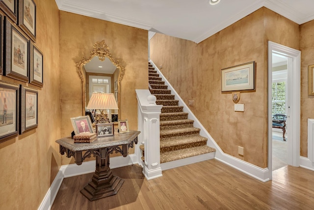 staircase featuring wood finished floors, ornamental molding, and baseboards