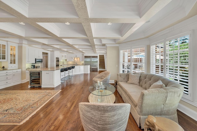 living area with beam ceiling, dark wood-type flooring, crown molding, coffered ceiling, and beverage cooler