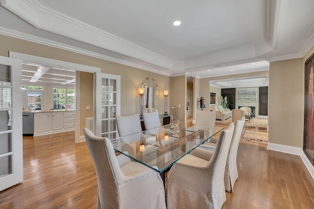 dining space featuring a raised ceiling, crown molding, and light wood-style flooring