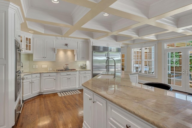 kitchen with beam ceiling, white cabinetry, stainless steel appliances, and a sink