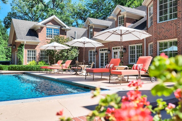 rear view of house with a patio, roof with shingles, an outdoor pool, and brick siding