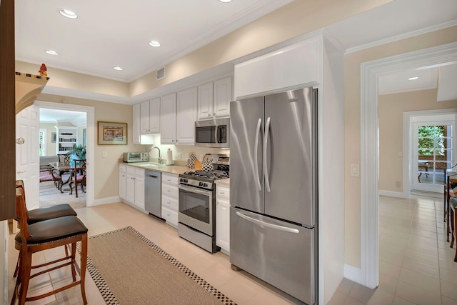 kitchen with white cabinets, stainless steel appliances, light countertops, baseboards, and ornamental molding