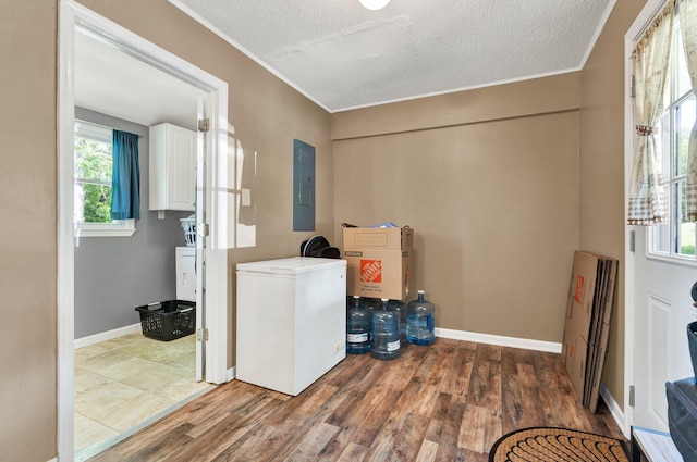 laundry room featuring a textured ceiling, electric panel, ornamental molding, cabinet space, and wood finished floors