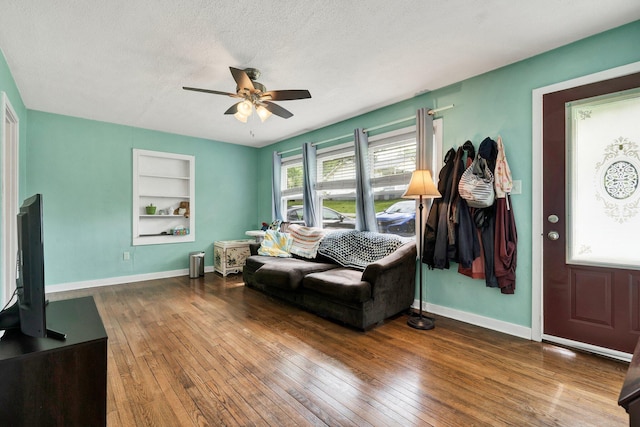 living area featuring hardwood / wood-style floors, built in shelves, ceiling fan, baseboards, and a textured ceiling