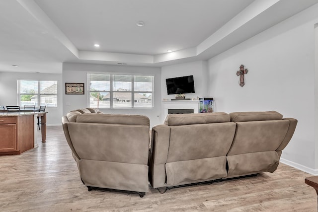 living room featuring baseboards, a fireplace, a tray ceiling, and light wood-type flooring