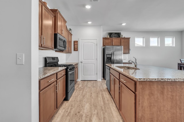 kitchen featuring light wood-type flooring, brown cabinets, a sink, backsplash, and stainless steel appliances