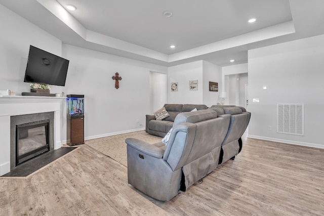living area featuring baseboards, a tray ceiling, visible vents, and wood finished floors