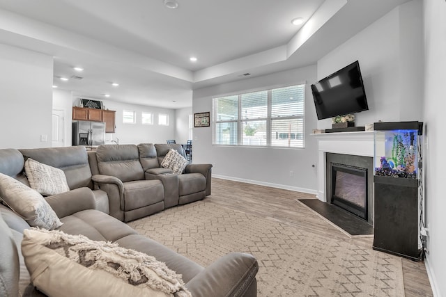 living room featuring a fireplace with flush hearth, baseboards, recessed lighting, and light wood finished floors