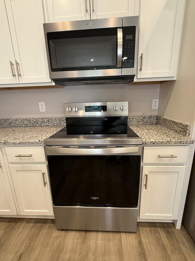 details with white cabinetry, light stone countertops, appliances with stainless steel finishes, and light wood-type flooring