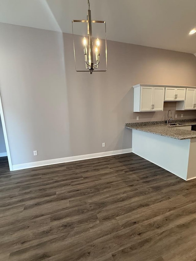 kitchen with white cabinetry, stone countertops, dark wood-style floors, baseboards, and a notable chandelier
