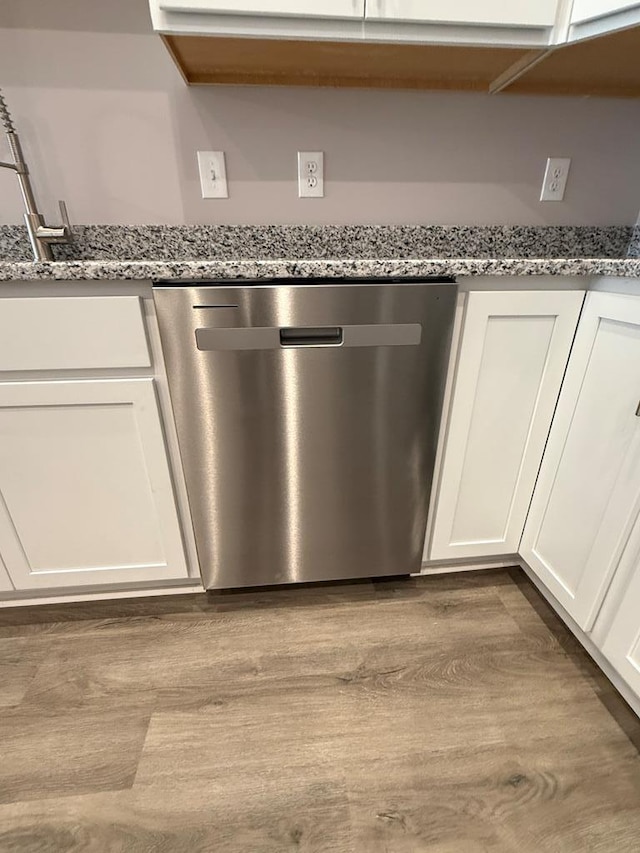 room details with dishwasher, white cabinets, light stone counters, and wood finished floors