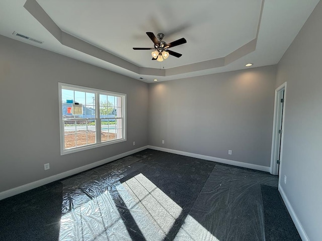 spare room featuring visible vents, baseboards, dark colored carpet, and a tray ceiling