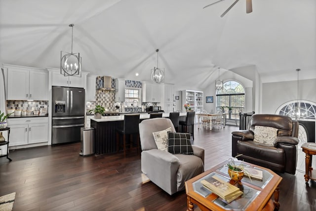 living area with ceiling fan with notable chandelier, dark wood-style flooring, and lofted ceiling