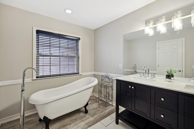 full bathroom with a sink, double vanity, a freestanding bath, baseboards, and wood finished floors