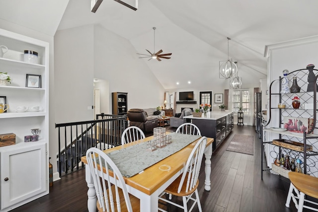 dining space featuring dark wood-style floors, a fireplace, built in shelves, high vaulted ceiling, and ceiling fan with notable chandelier