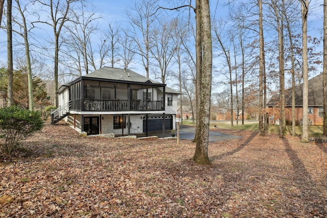 back of property featuring stairway, a shingled roof, an attached garage, and a sunroom