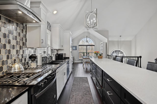 kitchen with stainless steel appliances, wall chimney range hood, a sink, white cabinetry, and a notable chandelier
