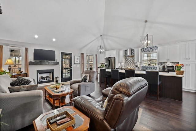 living area with recessed lighting, an inviting chandelier, a fireplace, dark wood-type flooring, and lofted ceiling