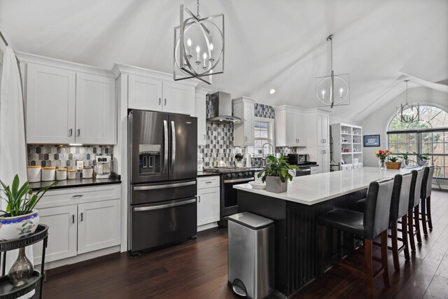 kitchen featuring an inviting chandelier, decorative backsplash, wall chimney range hood, refrigerator with ice dispenser, and gas range