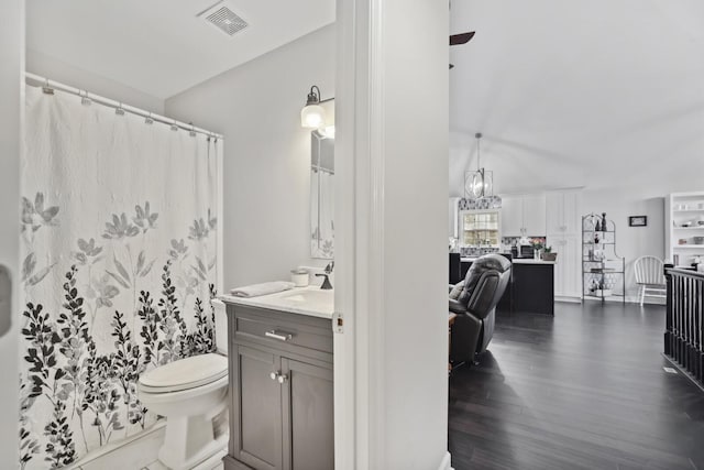 full bath featuring visible vents, toilet, wood finished floors, vanity, and a notable chandelier