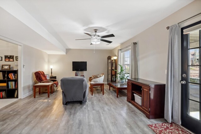 living area featuring a ceiling fan, light wood-style flooring, and baseboards