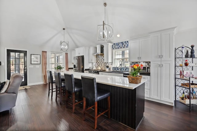 kitchen with an inviting chandelier, stainless steel fridge with ice dispenser, wall chimney range hood, a sink, and a kitchen breakfast bar