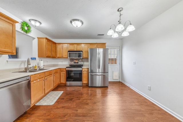 kitchen with an inviting chandelier, a sink, dark wood-type flooring, light countertops, and appliances with stainless steel finishes