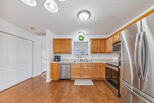 kitchen with brown cabinets, a sink, stainless steel appliances, light countertops, and dark wood finished floors
