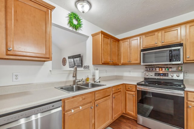 kitchen featuring a sink, stainless steel appliances, light countertops, vaulted ceiling, and wood finished floors