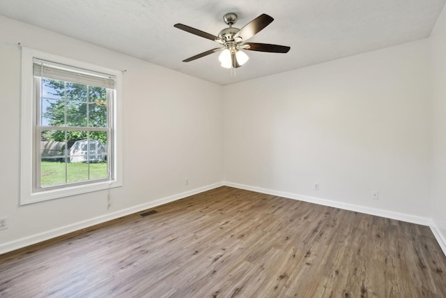 empty room with baseboards, a ceiling fan, wood finished floors, and visible vents