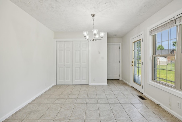 unfurnished dining area featuring an inviting chandelier, baseboards, a textured ceiling, and visible vents