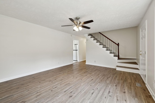 unfurnished living room featuring stairs, a ceiling fan, baseboards, and wood finished floors