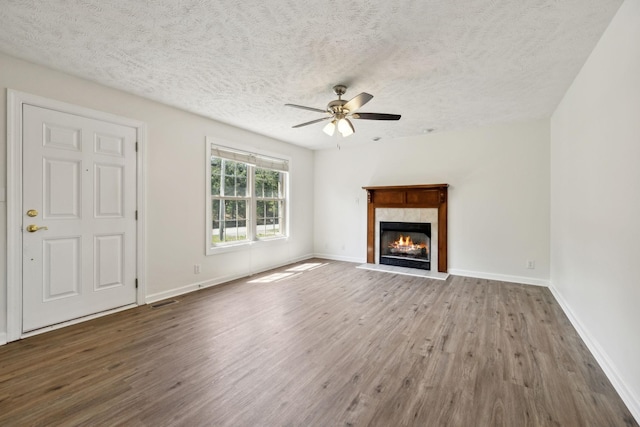 unfurnished living room featuring a ceiling fan, a textured ceiling, a tiled fireplace, and wood finished floors