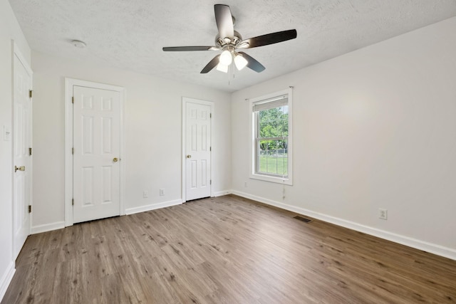 unfurnished bedroom featuring baseboards, a textured ceiling, visible vents, and wood finished floors