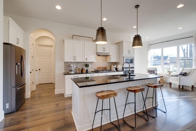 kitchen featuring decorative backsplash, a sink, appliances with stainless steel finishes, dark countertops, and under cabinet range hood