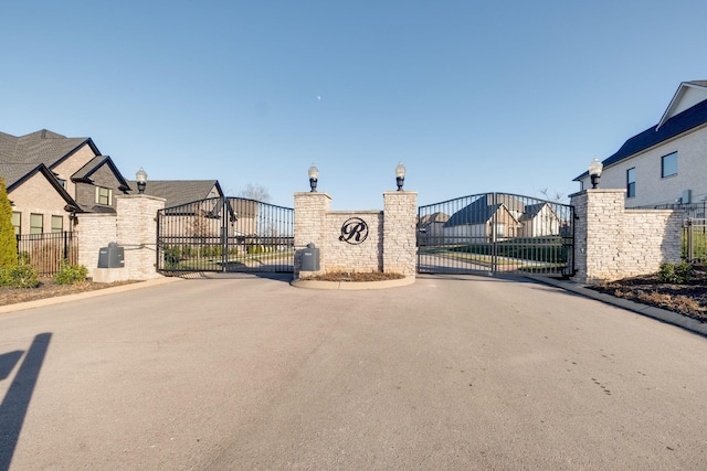 view of road featuring a gate, street lighting, curbs, and a residential view