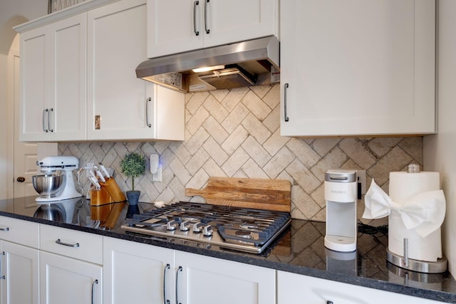 kitchen with exhaust hood, stainless steel gas stovetop, dark stone countertops, tasteful backsplash, and white cabinets