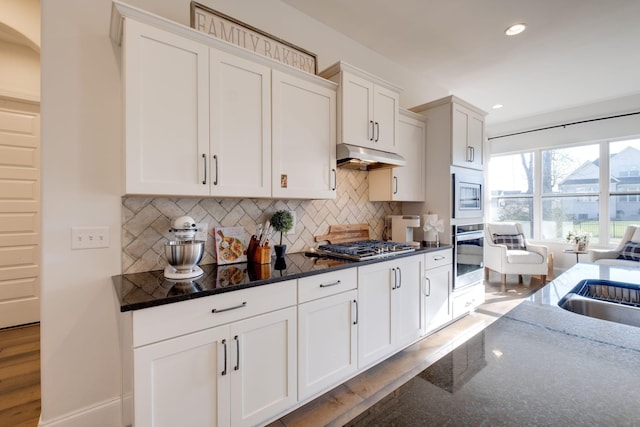 kitchen with recessed lighting, dark stone counters, stainless steel appliances, backsplash, and white cabinetry