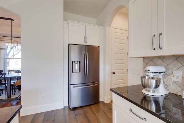 kitchen with dark wood finished floors, arched walkways, dark stone counters, stainless steel fridge, and backsplash