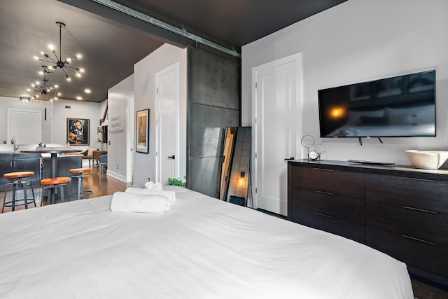 bedroom featuring dark wood-style floors, a sink, a barn door, a chandelier, and baseboards