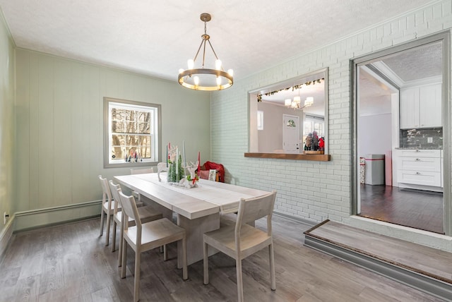dining area featuring brick wall, wood finished floors, a chandelier, and a baseboard radiator