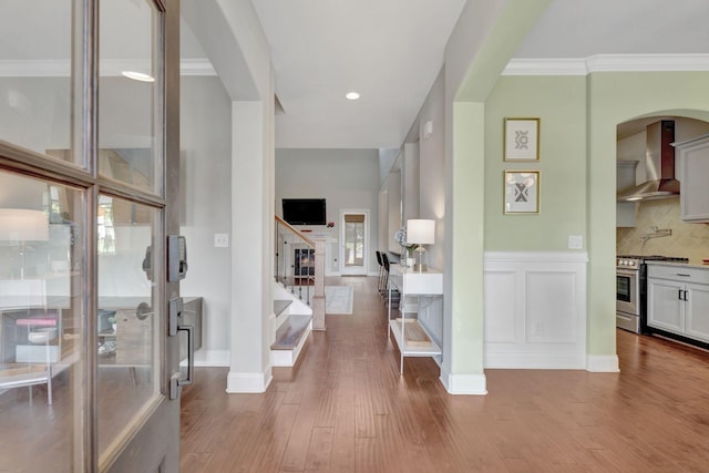 hall featuring stairway, wood finished floors, ornamental molding, and arched walkways