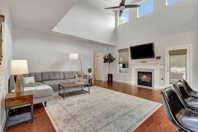 living room featuring a fireplace with flush hearth, arched walkways, dark wood finished floors, a ceiling fan, and a high ceiling