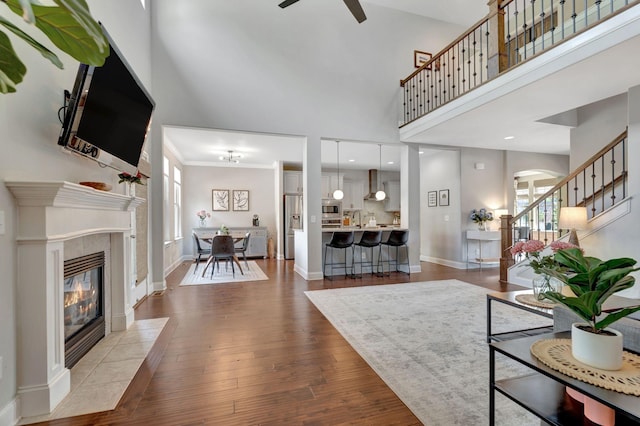 living room featuring dark wood finished floors, arched walkways, a tile fireplace, ceiling fan, and a towering ceiling