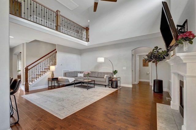 living area featuring arched walkways, wood finished floors, stairs, ceiling fan, and a high ceiling