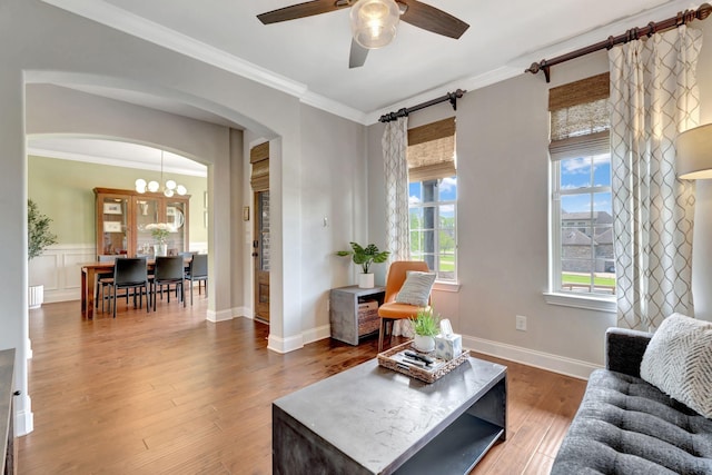 living area featuring wood finished floors, a healthy amount of sunlight, ornamental molding, and ceiling fan with notable chandelier