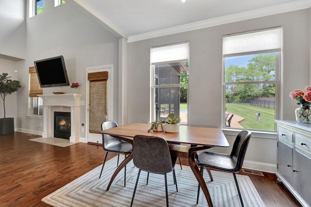 dining room featuring a fireplace with flush hearth, plenty of natural light, ornamental molding, and dark wood-style floors